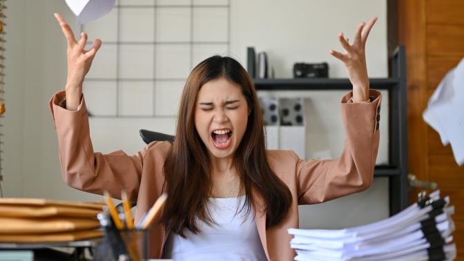 A woman is sat at her desk, shouting and throwing papers in the air