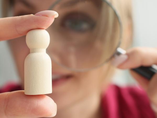 A woman examines a small wooden figure using a magnifying glass.