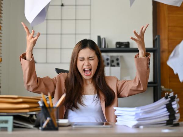 A woman is sat at her desk, shouting and throwing papers in the air